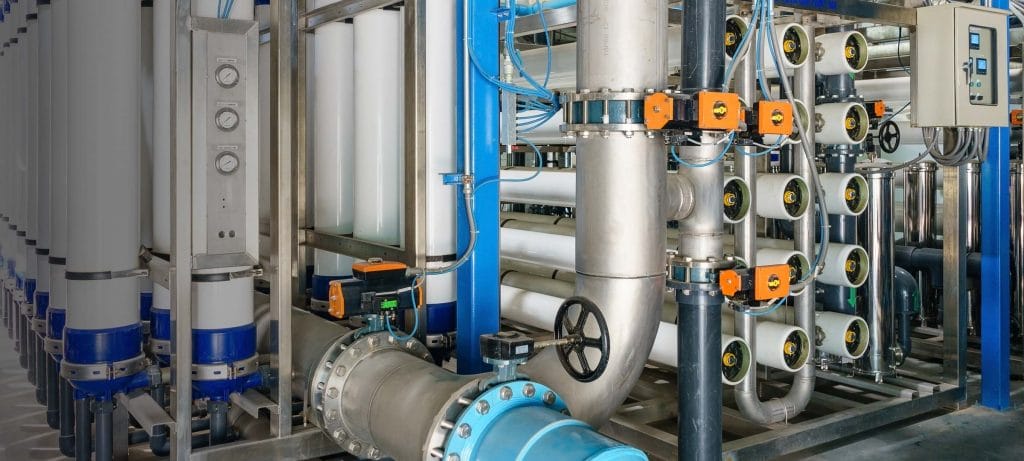 Industrial water filtration system with white pressure vessels and metal piping.